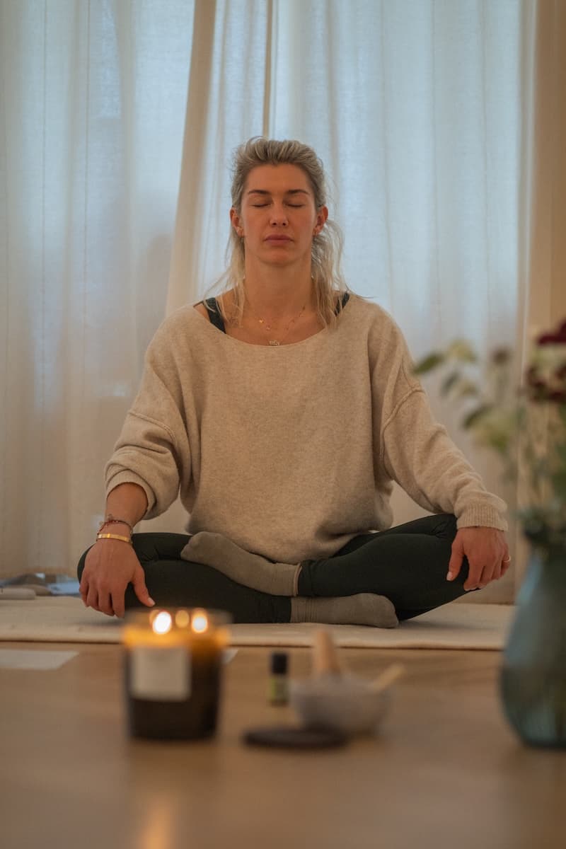 Dominique Scharax sitting cross-legged with her eyes closed, a candle burning in front of her